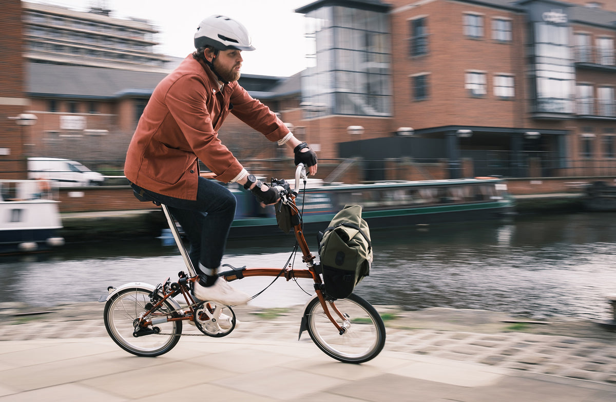 man riding a brompton bike in an urban environment, with restrap brompton bags attached