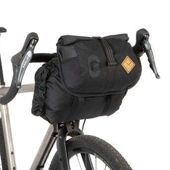 A black Restrap Holster Bar Bag Plus mounted on a bicycle handlebar, featuring a rolltop canister bag attached in front.
