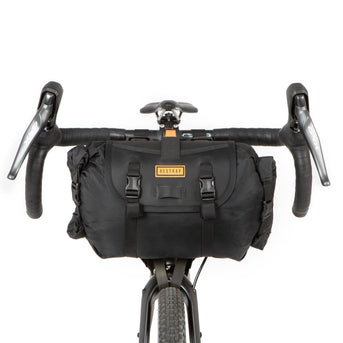 A black restrap holster bar bag attached to the handlebars of a bicycle, designed for bikepacking.