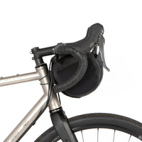 A black Race Bar Bag attached to the handlebars of a bicycle, featuring a holster system and a roll-top dry bag - this is attached to drop handlebars