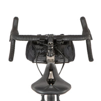 A black Race Bar Bag attached to the handlebars of a bicycle, featuring a holster system and a roll-top dry bag - this is attached to drop handlebars
