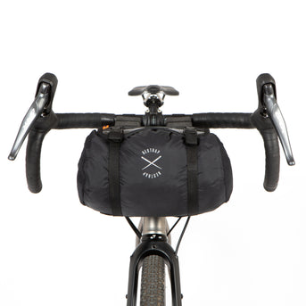 A black Race Bar Bag attached to the handlebars of a bicycle, featuring a holster system and a roll-top dry bag - this is attached to drop handlebars