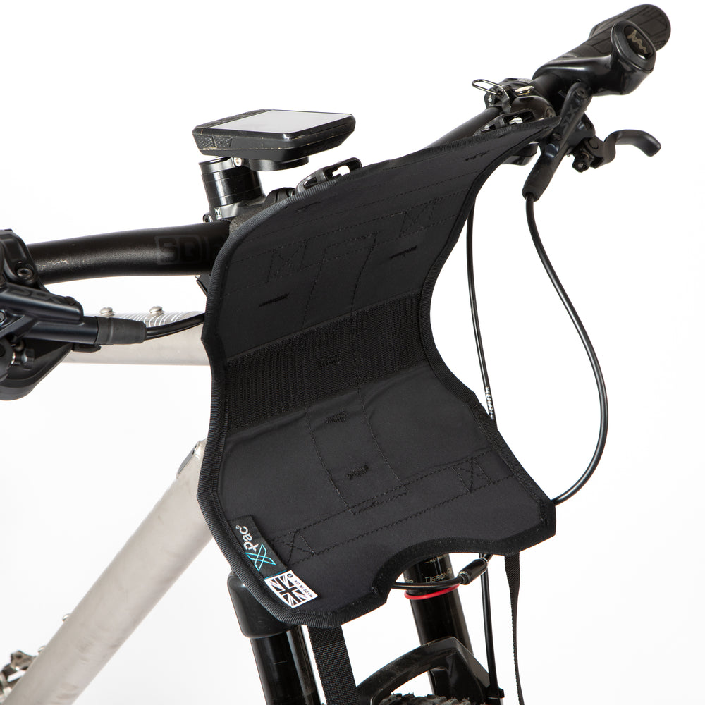 A black Race Bar Bag holster attached to the handlebars of a bicycle, featuring a holster system and a roll-top dry bag - this is attached to flat handlebars on a mountain bike