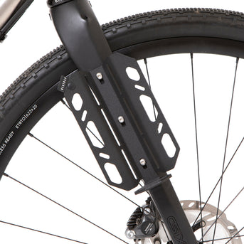 A black laser cut aluminium cargo cage mounted to the fork of a bicycle, with Restrap branded rubber label visible.