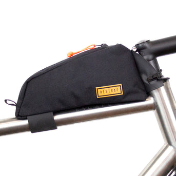A black Restrap top tube bag attached to the frame of a bicycle, designed to hold tools and snacks within reach.