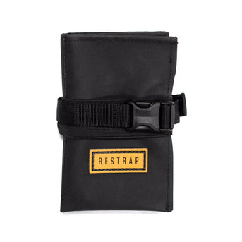 A black Restrap tool roll with a visible brand label, designed to be attached to a bicycle saddle or kept in a jersey pocket.
